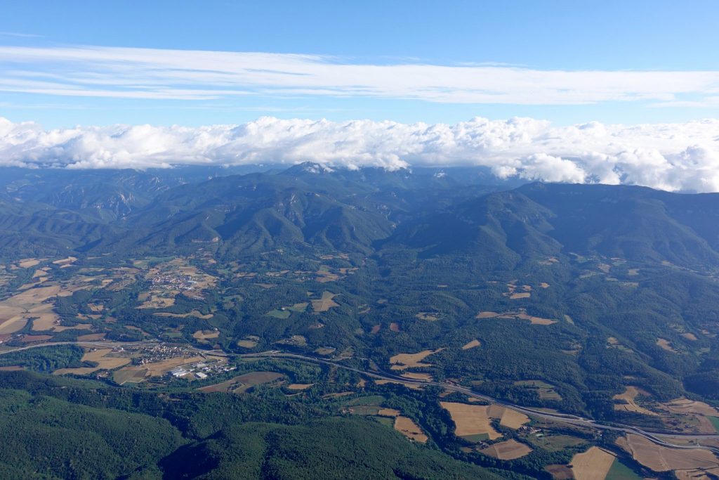 Landschaft der Garroxta von oben (im Heißluftballon): eine dicke Wolkendecke liegt über den grünen Hügel der Garroxta; dazwischen sind gelbe Felder