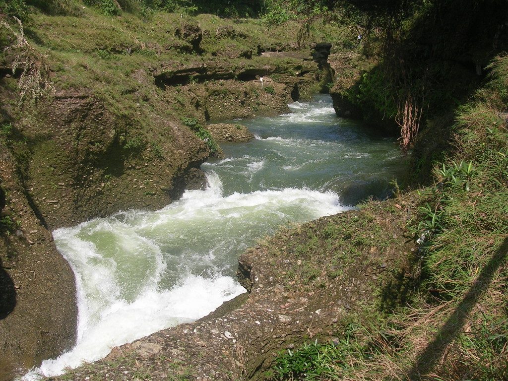 Der Pedi Khola kurz bevor er beim Devi´s Falls in die Tiefe stürzt: zwischen zwei braunen Uferseiten ist der grüne Fluss zu sehen mit vorne weiß schäumender Gischt