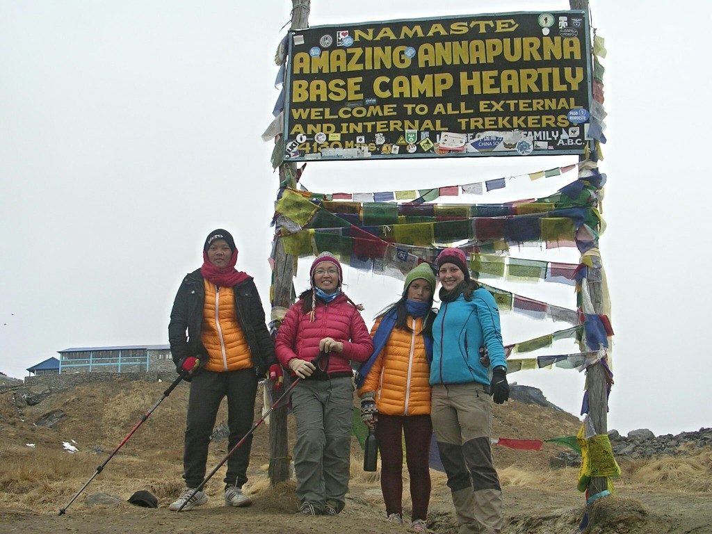 Sun Maya, Palee, Uti und ich stehen vor dem Annapurna Base Camp Schild, auf dem steht: "Amazing Annapurna Base Camp Heartly Welcome to all external and internatal trekkers" auf 4200m; der Himmel ist ganz weiß vor Nebel